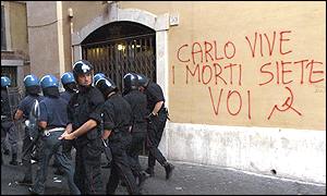 Riot police walk past a wall bearing graffiti referring to young protestor Carlo Giuliani who was shot dead during the protests